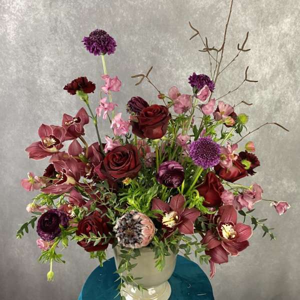 Large burgundy and pink floral arrangement in a white urn vase