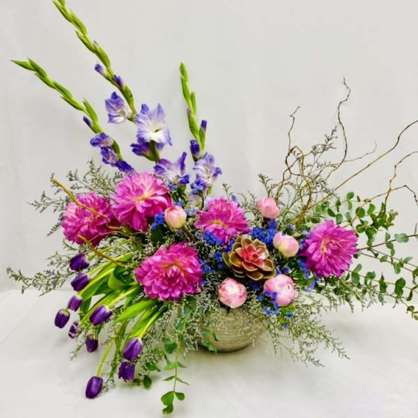 Bright mixed flower arrangement in a low bowl with pink, purple, and blue blooms