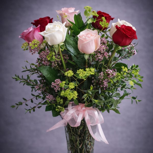 Mixed roses in a tall glass vase with a pink ribbon