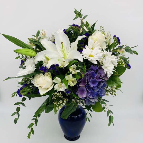 White and purple mixed flower arrangement in a navy blue vase