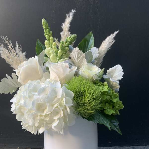 White floral arrangement in a pale cylindrical vase with green accents