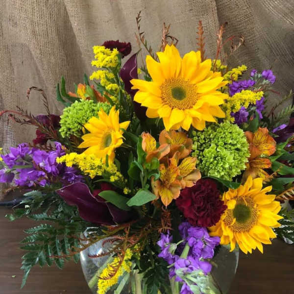 Mixed bouquet with sunflowers, purple blooms, and green hydrangea in a glass vase
