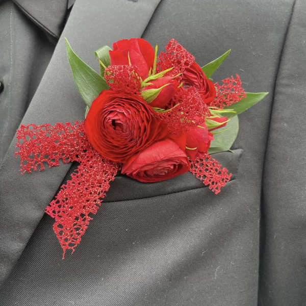 Red rose boutonniere with green leaves and glittery red ribbon on a dark suit