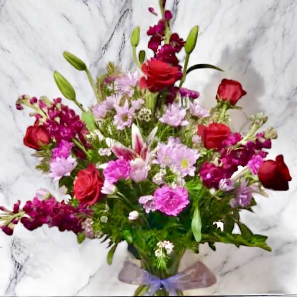 Mixed bouquet of pink and red flowers with a purple ribbon
