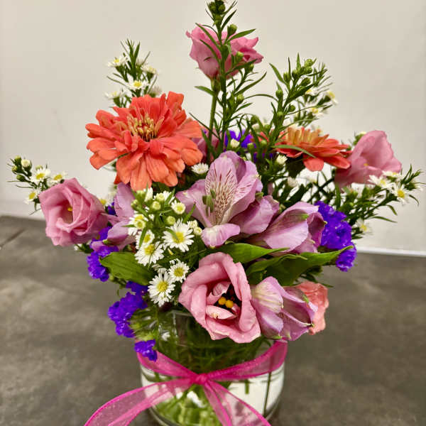 Mixed pink and orange flowers in a glass vase with a pink ribbon