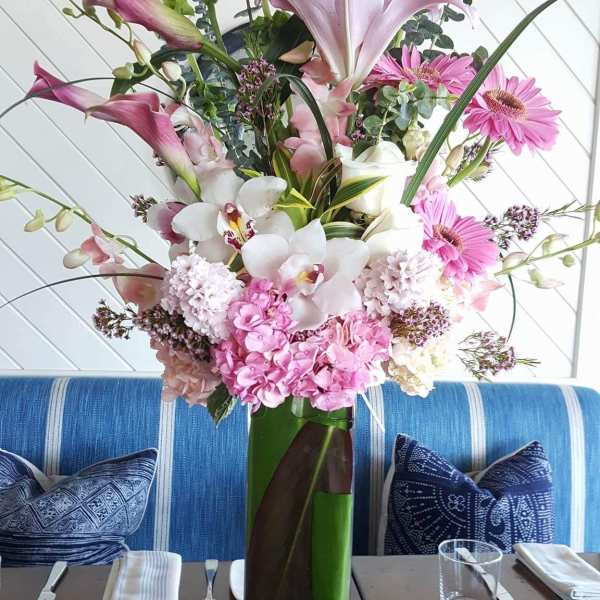 Tall pink and white floral arrangement in a glass vase on a dining table