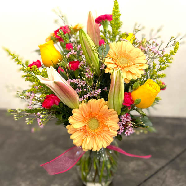 Mixed bouquet with yellow roses, peach gerberas, and pink lilies in a glass vase
