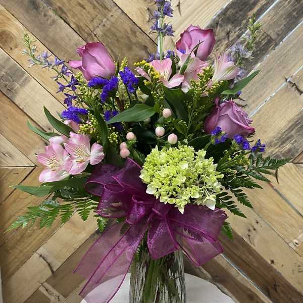 Bouquet of pink roses and mixed blooms in a glass vase with a purple ribbon