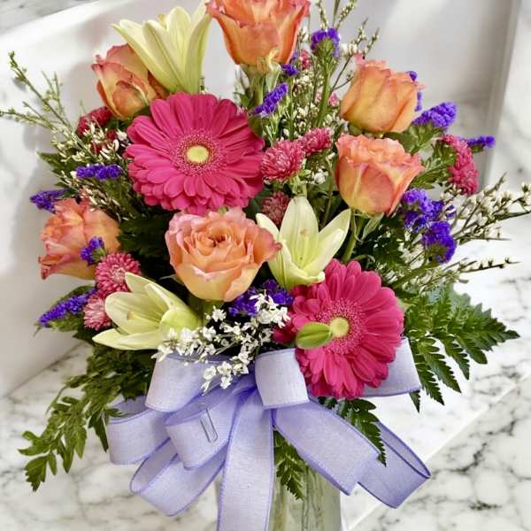 Bouquet of pink gerbera daisies, peach roses, and white lilies with a lavender ribbon