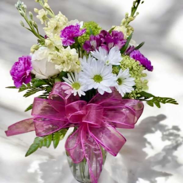 Bouquet of white daisies and pink flowers in a glass vase with a pink ribbon