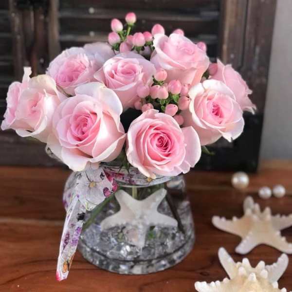 Pink roses arranged in a clear glass vase with a patterned ribbon