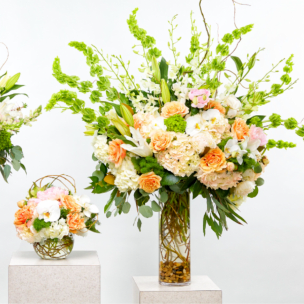 Three pastel floral arrangements in glass vases on white pedestals