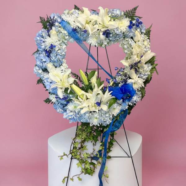 Heart-shaped floral wreath with white lilies and blue flowers on a stand