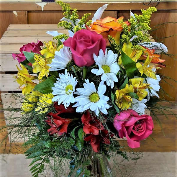 Mixed bouquet of roses, daisies, and yellow alstroemeria in a glass vase