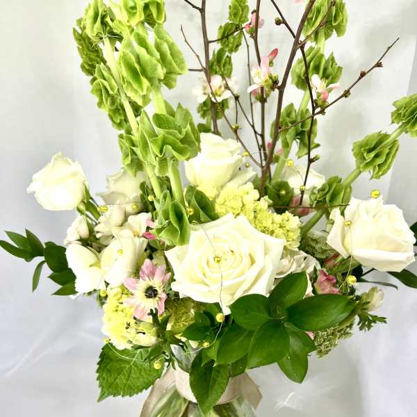 White roses and pink blossoms in a glass vase with tall green stems