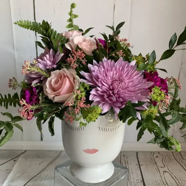 Pink and lavender flowers arranged in a white face vase