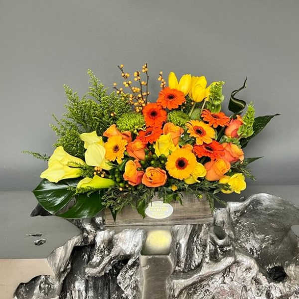 Bright mixed bouquet with yellow calla lilies, orange gerberas, and roses in a wooden box