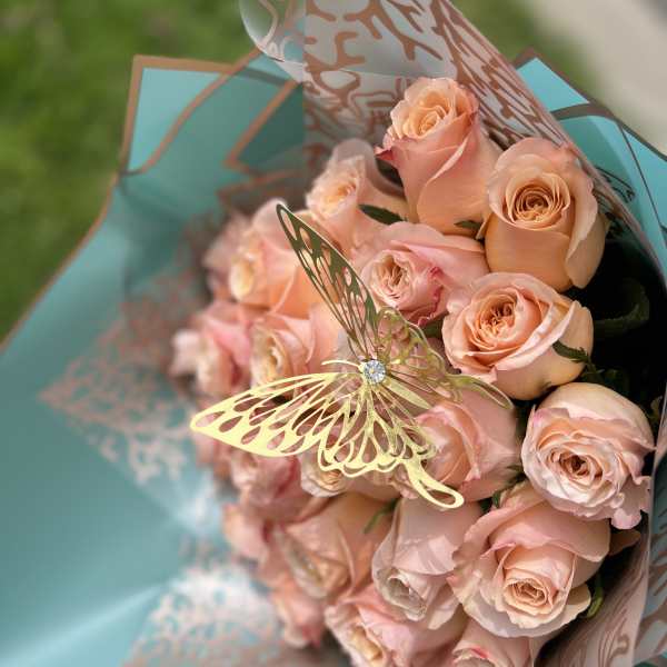 Bouquet of pale peach roses wrapped in turquoise paper with a butterfly pick