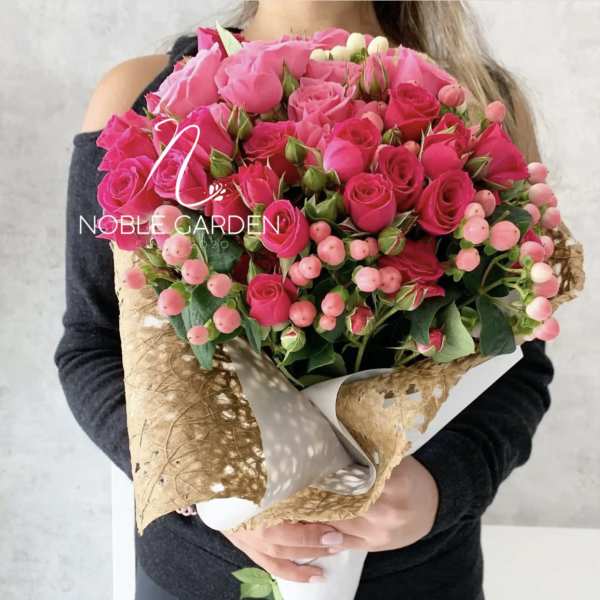 Bouquet of bright pink roses with pink berries wrapped in tan paper