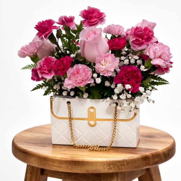 Pink carnations and roses arranged in a white handbag-shaped container