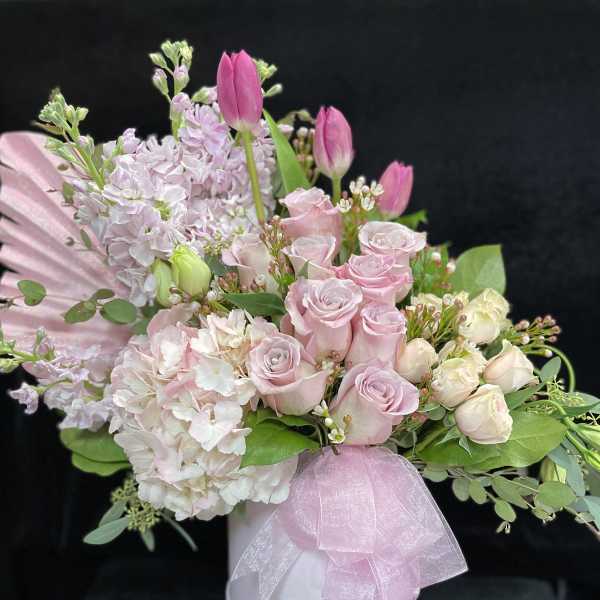 Pink roses and tulips arranged in a white hat box with a pink ribbon