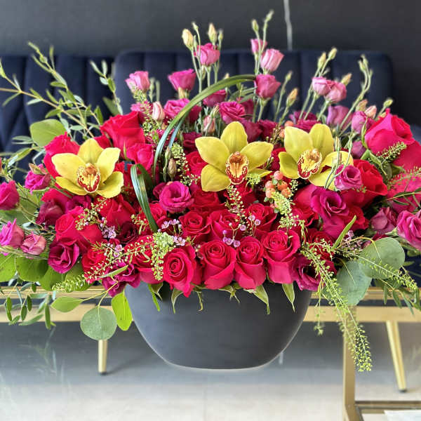 Pink and red roses with yellow orchids in a black bowl vase