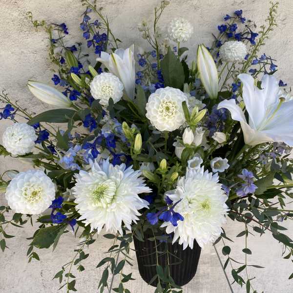 White lilies and blue flowers arranged in a black vase