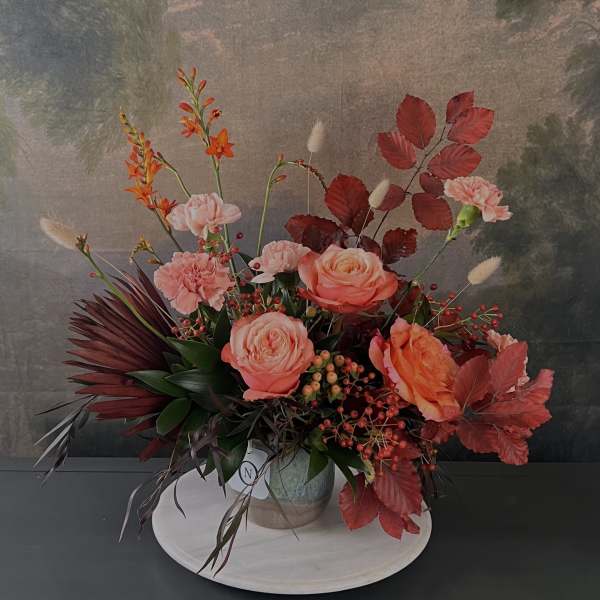 Arrangement of peach roses, pink carnations, and orange blooms in a vase