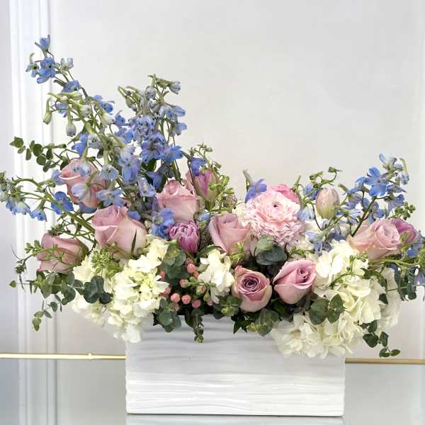 Pink roses and blue delphinium in a white rectangular vase