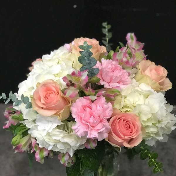 Bouquet of pink roses, white hydrangeas, and carnations in a glass vase