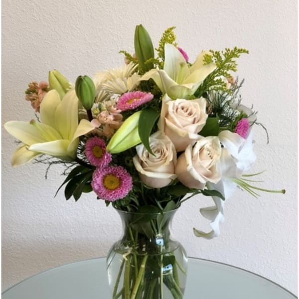 Bouquet of cream lilies, roses, and pink daisies in a glass vase