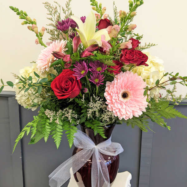 Mixed bouquet of roses, lilies, and daisies in a vase with a white ribbon