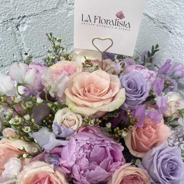 Pastel bouquet of roses and purple blooms with a florist card