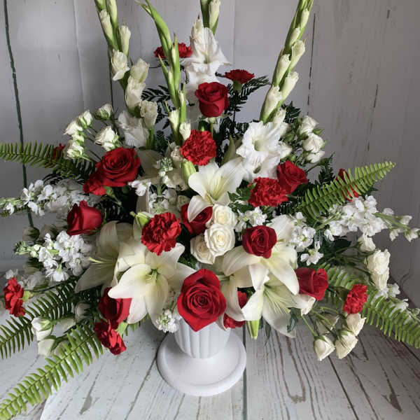 Red and white floral arrangement in a white pedestal vase