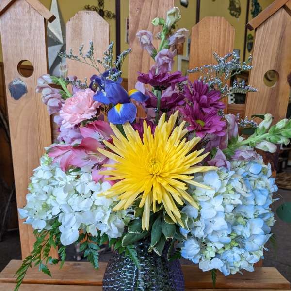 Mixed bouquet in a dark glass vase with yellow, pink, purple, and blue flowers