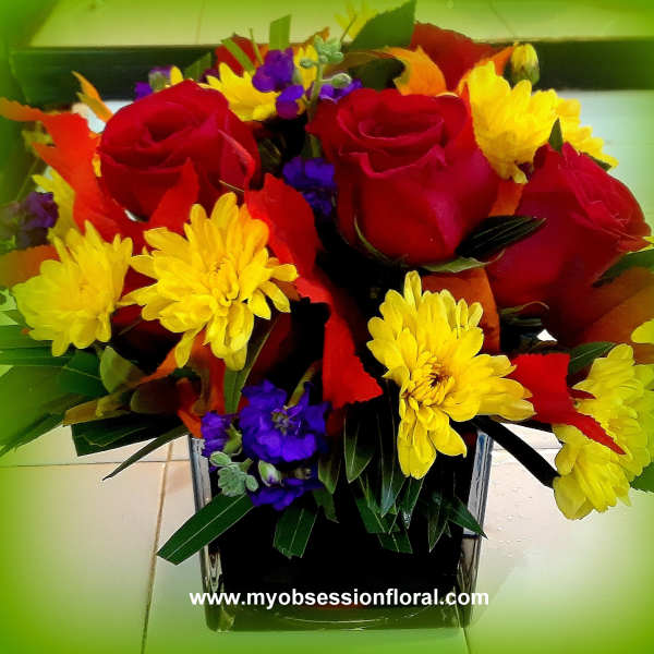 Bouquet of red roses and yellow daisies in a square glass vase