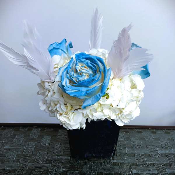 Blue rose and white hydrangea arrangement in a black vase with white feathers