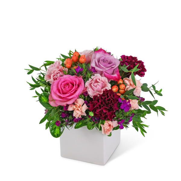 Pink and purple rose arrangement in a white square vase