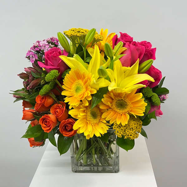 Mixed bouquet of yellow lilies, pink roses, and orange gerbera daisies in a glass vase