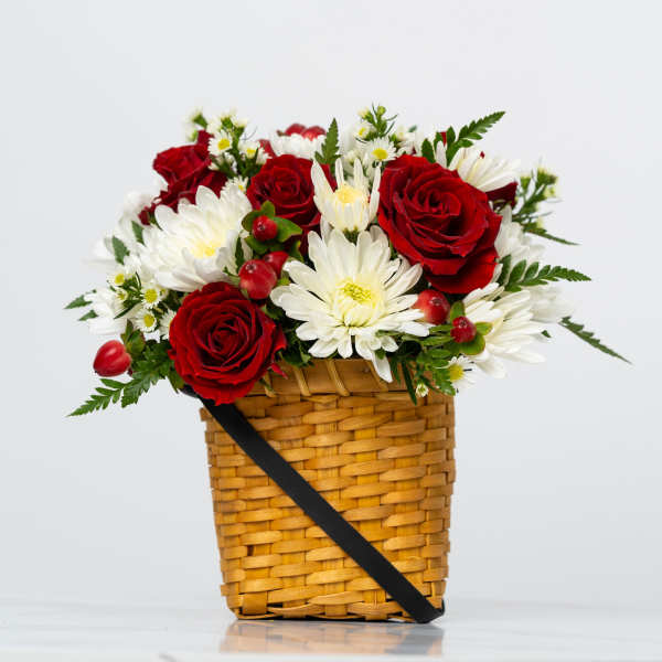 Red roses and white daisies in a woven basket with a black ribbon