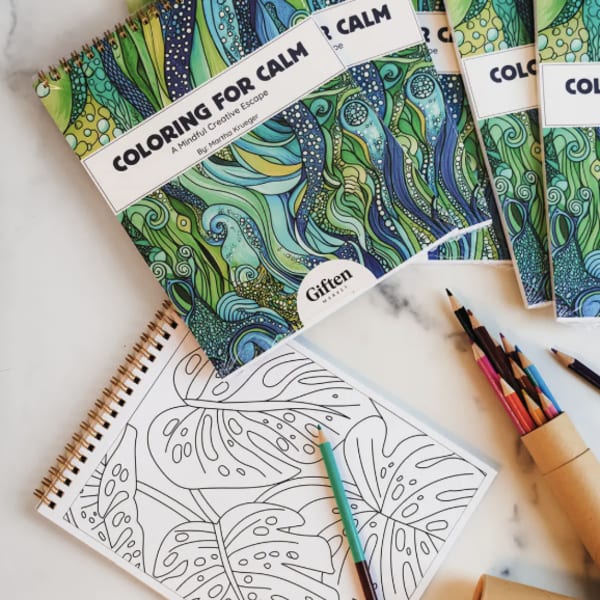 Coloring books and colored pencils arranged on a light surface