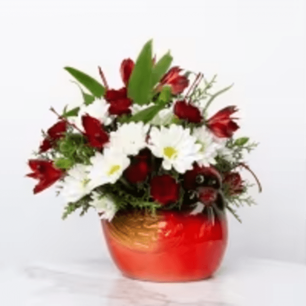 Red and white flower arrangement with daisies and roses in a round red ceramic bowl