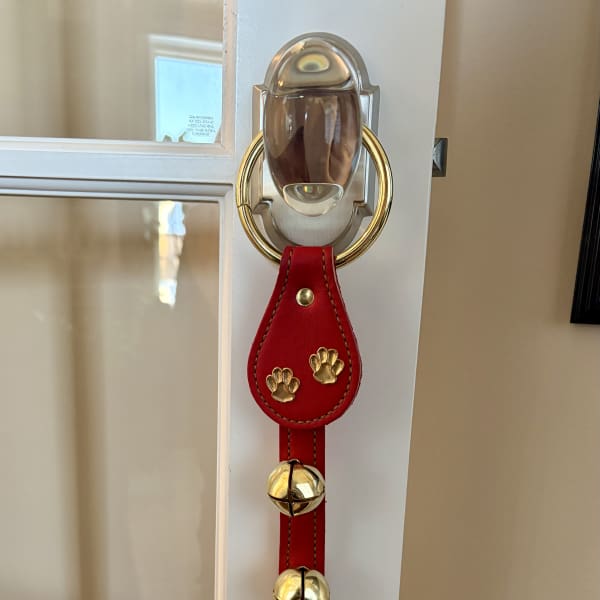 Red leather door hanger with gold paw prints and bells on a white door