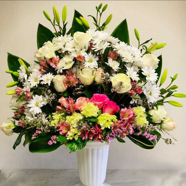 Tall mixed arrangement of white daisies, roses, lilies and pink flowers in a white pedestal vase
