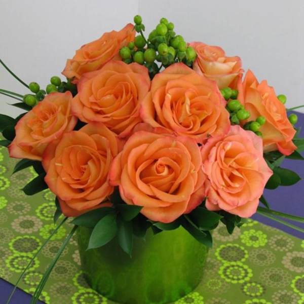 Compact arrangement of orange roses with green berries in a bright green cylinder vase.