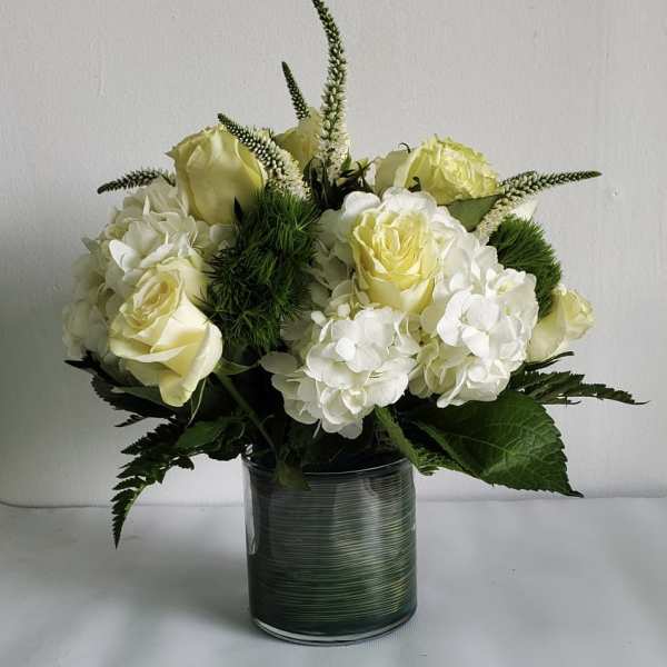 White and pale yellow roses with white hydrangeas in a glass vase