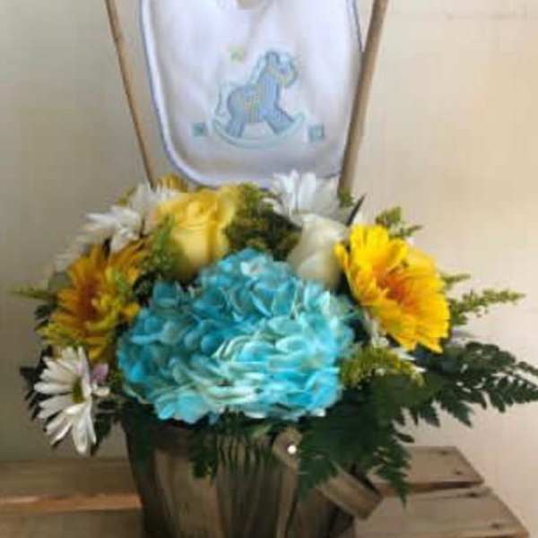 Colorful flower arrangement in a wooden basket with a baby bib on sticks