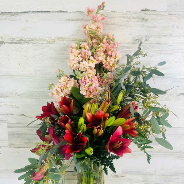 Tall bouquet of red lilies and pale pink flowers in a glass vase