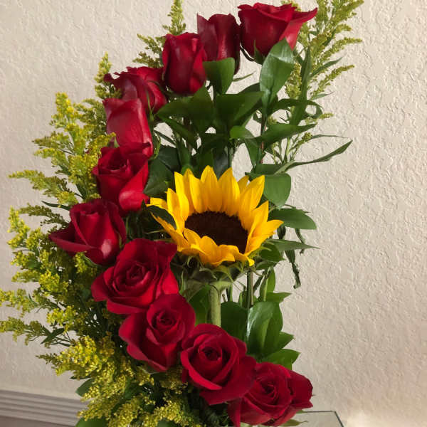 Arrangement of red roses and a yellow sunflower in a green glass vase