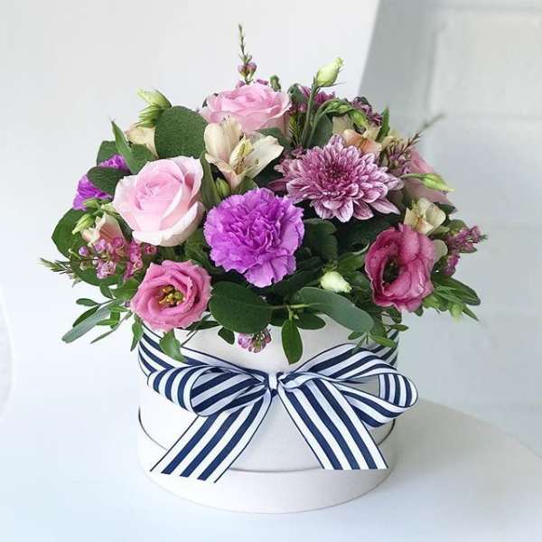 Pink and purple flowers arranged in a white round box with a striped ribbon